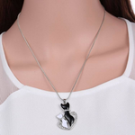 bigger crystal black cat and smaller crystal white cat in a crystal heart pendant hanging from a silver chain on a woman's neck
