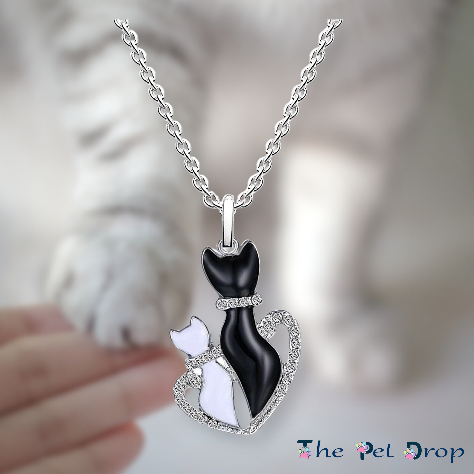 bigger crystal black cat and smaller crystal white cat in a crystal heart pendant hanging from a silver chain.