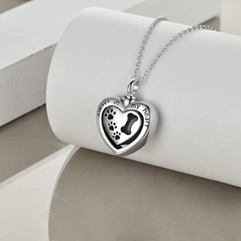 silver heart urn with black dog paw prints on it and the words "always in my heart" on the front  hanging on a silver chain.