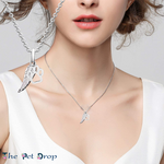 silver angel wing with a small silver paw print hanging from a silver chain on a woman's neck.