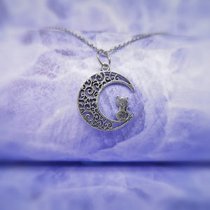 silver patterned moon pendant with a cat sitting on it hanging on a silver chain.