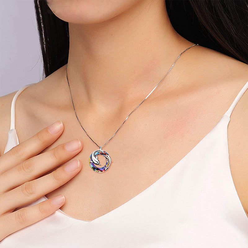 colourful crystal circle with one silver dolphin and a smaller rose gold dolphin in and around the circle pendant hanging on a silver chain on a woman's neck.