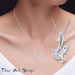 one silver dolphin with another little silver dolphin attached onto it with a clear crystal in between the two dolphins tail on a woman's neck.