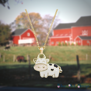 gold outlined white cow with a pale pink nose and 3 black patches hanging on a gold chain