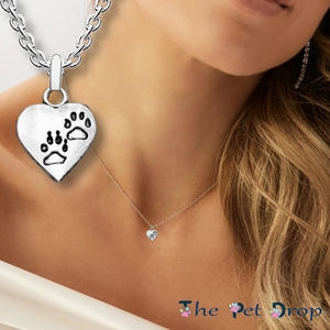 silver heart with two identical black outlined paw prints one above the other on a silver pendant hanging on a silver chain on a woman's neck.